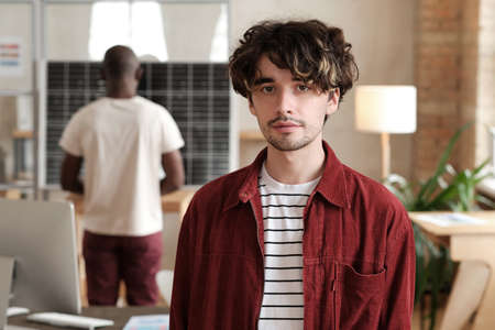 Portrait of young designer looking at camera while working at office with his colleaguesの写真素材