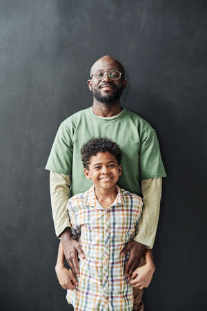 Portrait of African father smiling at camera together with his little son isolated on black...