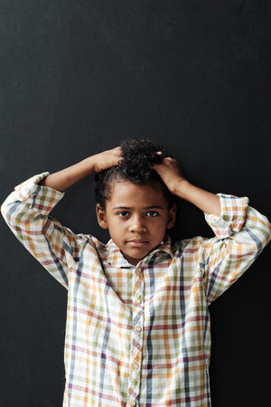 Portrait of African little boy with curly hair posing at camera against the black backgroundの写真素材