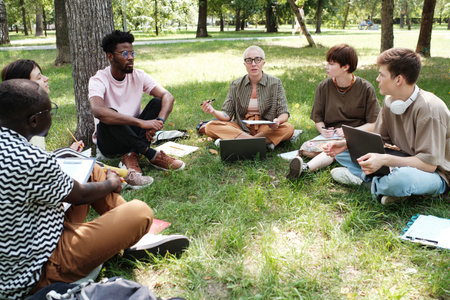 Group of students sitting on the grass and listening to their teacher they studying in the park outdoorsの写真素材