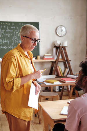 Teacher in eyeglasses talking to student during the lesson in the classromの写真素材