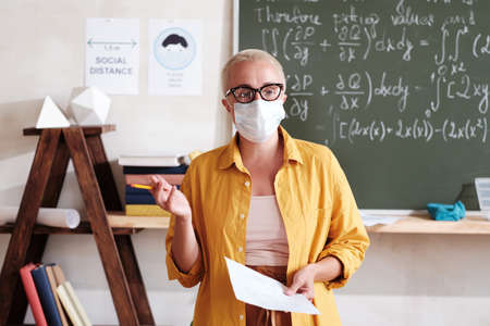 Portrait of young teacher in protective mask explaining new material while standing in the classroomの写真素材