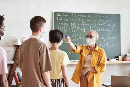 Teacher in mask with medical equipment holding medical exam for students before lesson at schoolの写真素材