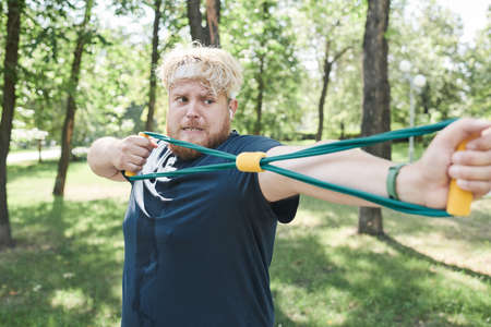 Overweight man exercising with sports equipment and doing stretching exercises during training in the parkの写真素材