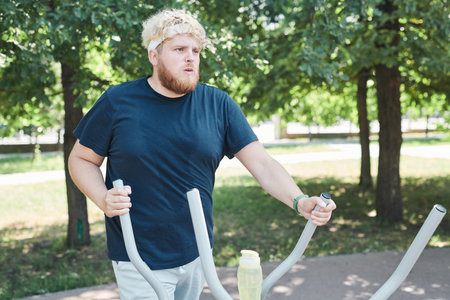 Overweight young man exercising on sports equipment in the parkの写真素材