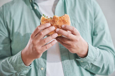 Close-up of man holding burger in his hands to eat it for lunchの写真素材