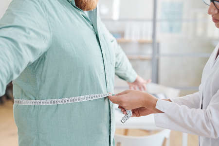 Close-up of doctor measuring waist of overweight man during his visit to the hospitalの写真素材