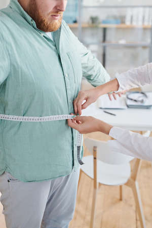 Close-up of nutritionist measuring the waist of her patient with tape measure during his visit at hospitalの写真素材