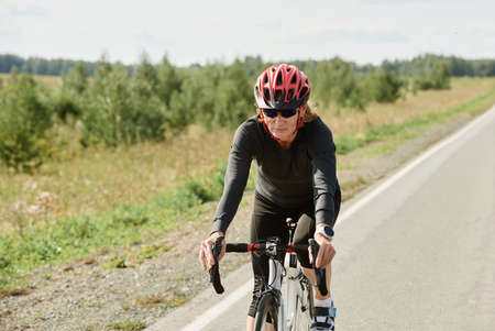 Woman in helmet and in sports clothing racing on bike on a road outdoorsの写真素材