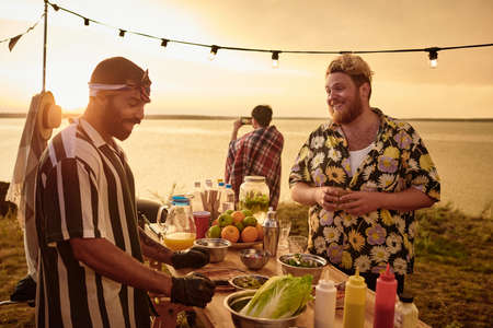 Young people talking to each other and eating fast food during sunset at party on the beach