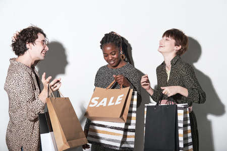 Group of young friends with shopping bags looking excited and happy after shopping while standing...