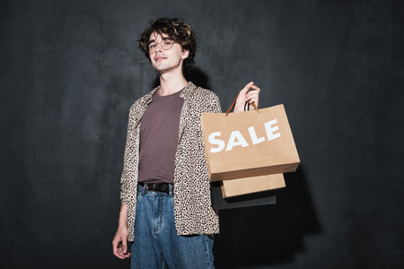 Portrait of young stylish man with paper bags looking at camera standing against the black backgroundの写真素材