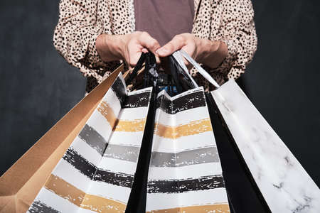 Close-up of customer holding shopping bags with purchases in his hands isolated on black backgroundの写真素材