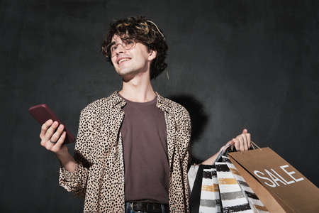 Young man with shopping bags using mobile phone for online shopping isolated on black backgroundの写真素材