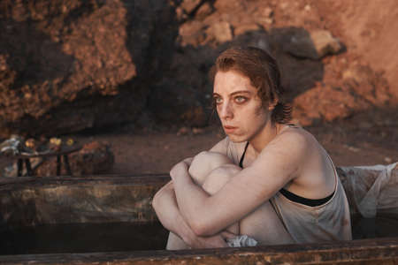 Young depressed woman sitting in dirty bath looking at sunset and thinking about something outdoors