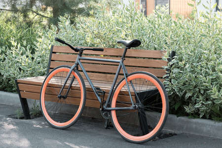 Horizontal no people shot of modern bicycle parked outdoors against wooden bench in city park on...