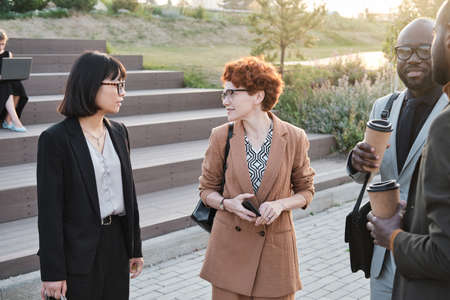 Group of modern business people standing together in urban park relaxing, drinking coffee and talking to each other during coffee breakの写真素材
