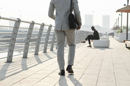 Horizontal back view shot of unrecognizable man wearing suit walking along street somewhere in modern cityの写真素材