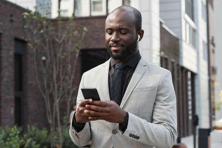 Horizontal medium portrait of joyful African American man with beard on face wearing earbuds...