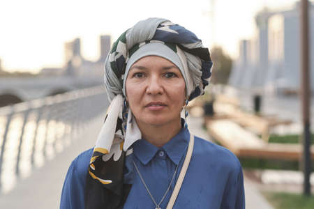 Portrait of mature muslim woman with scarf on her head looking at camera standing in the cityの写真素材