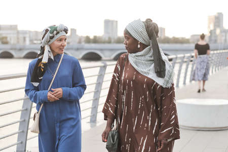 Two young women in muslim clothes talking to each other during their walk in the cityの写真素材