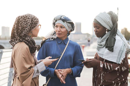 Group of muslim women using their mobile phones and discussing online apps while standing in the cityの写真素材