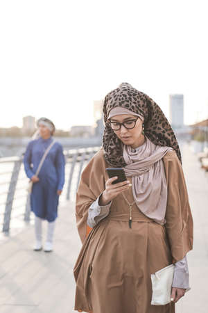 Young muslim woman texting a message on her mobile phone while walking in the cityの写真素材