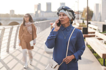Elegant muslim woman talking on mobile phone while walking along the street in the cityの写真素材