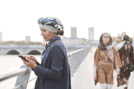 Elegant muslim businesswoman working online on mobile phone while standing in the cityの写真素材