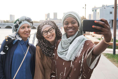 Happy muslim women standing in the city and smiling at camera they using mobile phone to make selfie portraitの写真素材