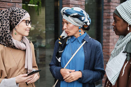 Elegant muslim women talking to each other while standing on the street during their meetingの写真素材