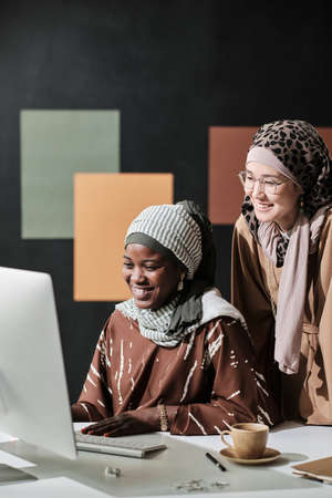 Two muslim businesswomen working together at the table at office they looking at computer monitor and laughingの写真素材