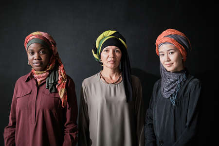 Portrait of three elegant women in hijabs looking at camera standing against the black backgroundの写真素材