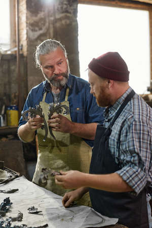 Man holding metallic detail in his hands and showing to his colleague the process of creationの写真素材