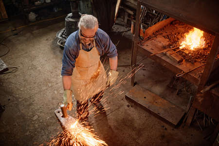 High angle view of mature man in apron forging the metal in the blacksmith shopの写真素材