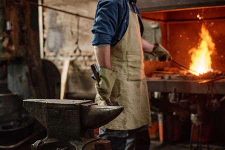 Close-up of worker adding coal in furnace while working with hammer in the blacksmith shopの写真素材