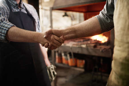 Close-up of two workers standing and shaking hands during their work in workshop