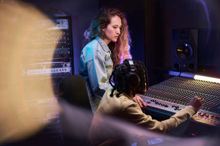 African young producer using music keyboard to write a song for singer in the recording studioの写真素材