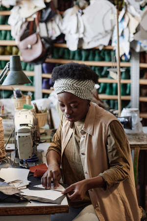 African young tailor using patterns to cut clothes at her workplace in the clothes factoryの写真素材