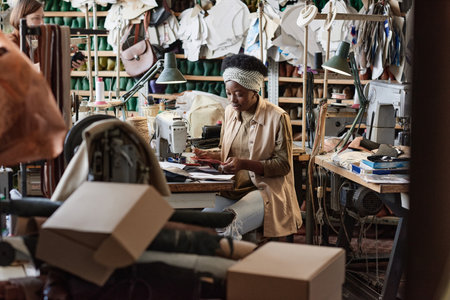 African dressmaker working at the table with fabric to sew new products in the workshopの写真素材