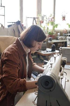 Serious tailor sewing clothes on sewing machine while working in the factoryの写真素材