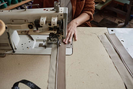 Close-up of female fashion designer working on sewing machine creating new clothing line in design...