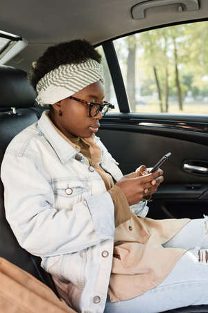 African businesswoman using her mobile phone during her trip in the car