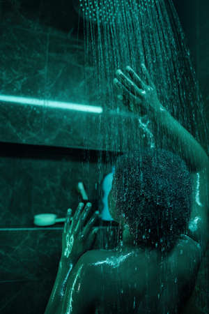 Rear view of African woman standing under the shower and washing her body in the bathの写真素材