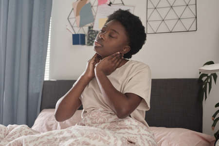 African young woman touching her neck and warming up after deep sleep in the bedroomの写真素材