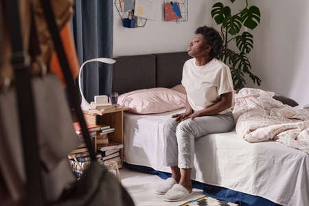 African young woman sitting on the bed in the morning and looking at windowの写真素材
