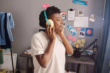 African young woman with closed eyes enjoying the music in wireless headphones while standing in the...