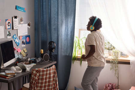 African girl in headphones having fun in her room, dancing to music