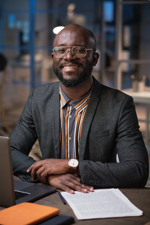 Portrait of African manager smiling at camera while working at his table with business documents...