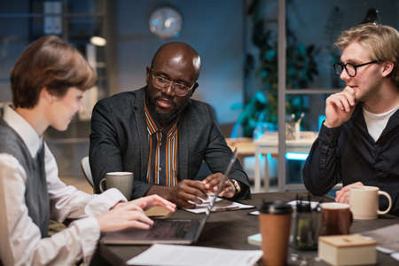 Group of business people sitting at the table discussing and using laptop at work during their...